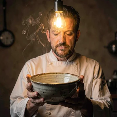Episode tile portrait of a former chef holding a worn ceramic bowl, single warm 