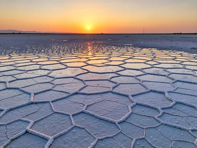 Salt flat hexagonal patterns stretching to horizon, sunset reflection in thin wa