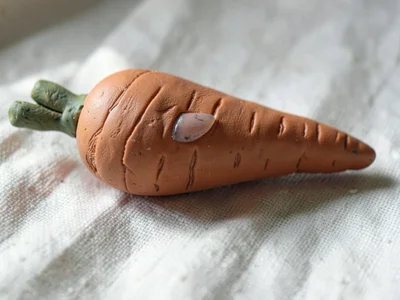 Gleaned terracotta carrot with a slumped tip and fingernail-grooved skin, on pla