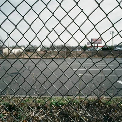 Close-up of a chain-link fence section with a parking lot and distant retail sig