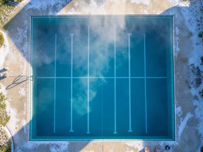 A lap pool at dawn from above, steam rising from the heated water creating a haz