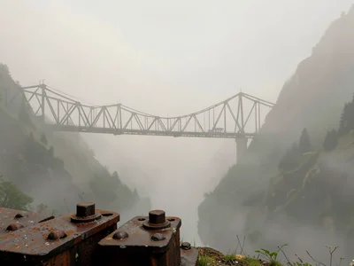 Iron trestle spanning a fogged-in valley, bolts and rivets at the foreground, th