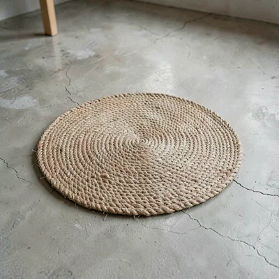 A single round woven jute mat placed centrally on washed concrete, fibers radiat