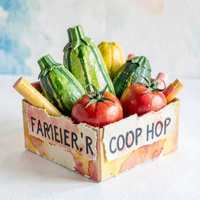 A pop-up paper farmers' co-op with torn-paper crates of crayon zucchini and toma