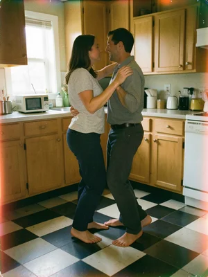 A couple slow-dancing in a kitchen, bare feet on checkered floor, a radio on the