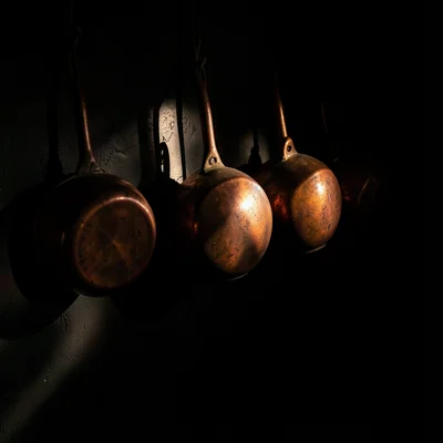 A row of copper pots hanging on a dark wall, each catching a different amount of