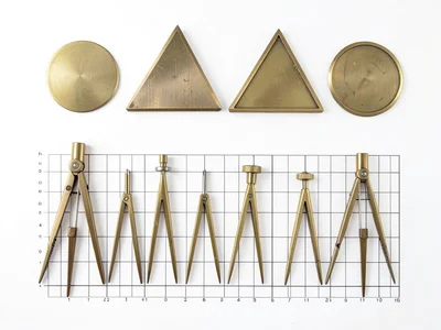 Row of drafting compasses arranged by size, brass on white background, top-down 