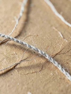 Fiber-warp threads bent across kraft tan as warm pulp catches grazing studio lig
