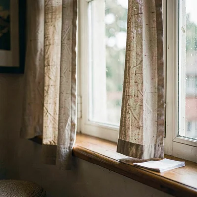 intimate window seat with linen curtains and a paper stack on the sill