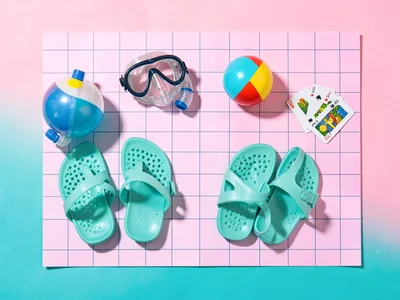 Top-down knolling grid of a snorkel mask, beach ball, jelly sandals, and playing