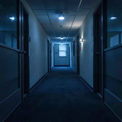 Empty office corridor at 3am with motion-sensor lights flickering on, deep navy