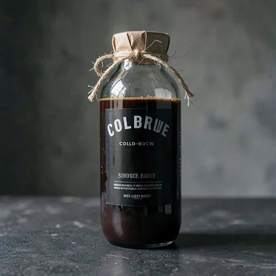 Lightbox three-quarter shot of a glass cold-brew bottle with a paper-twine cap,