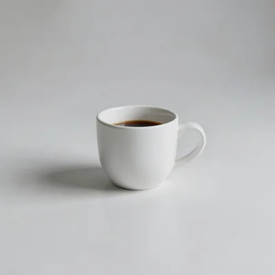 Minimalist photograph of a single white coffee cup on a clean matte surface, soft natural window light, subtle shadow, l