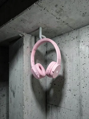 Pink gaming headphones hung on raw concrete nail, industrial texture versus soft