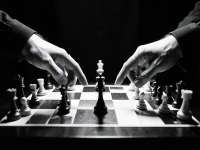 A chess match, two players' hands reaching for pieces simultaneously, the board 