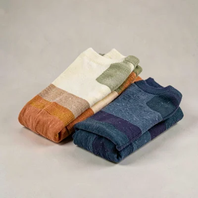 Lightbox three-quarter shot of three folded sock pairs in graduated colors, neut