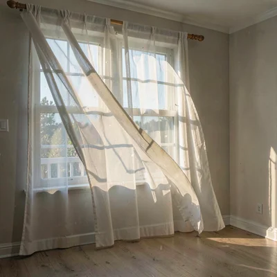 An empty room with sheer curtain billowing inward, afternoon light creating soft
