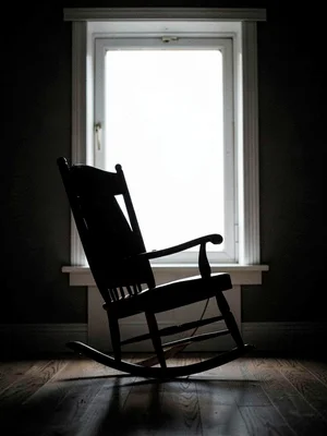 An empty rocking chair silhouetted against a bright window, absence present