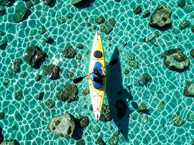 A kayaker from above on a crystal-clear lake, the boat and paddle creating a cro
