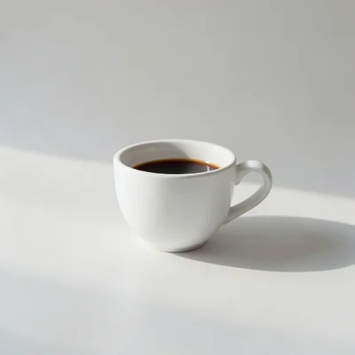 Minimalist photography of a single white coffee cup on a clean matte surface, soft natural window light, subtle shadow, 