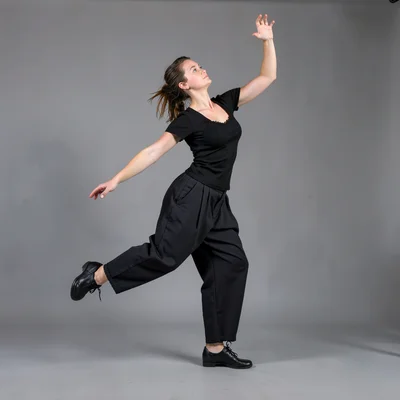 A dancer in rehearsal clothes against seamless gray, caught mid-turn