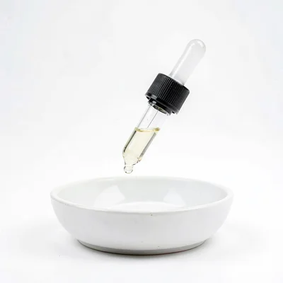 Minimal studio shot of a single glass dropper suspended over a porcelain dish, p