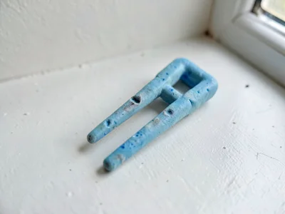 Chimed faded-blue tuning fork with a slumped handle and thumb dents along its ti