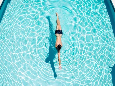 A single swimmer mid-freestyle in a 50m pool, body stretched long, one arm reach