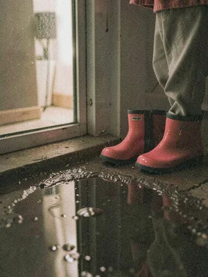 Child's rain boots left by a screen door, puddle reflecting bare bulb light, hea