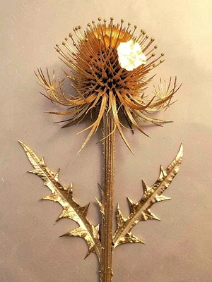 A dried thistle head with gold covering the spines and seed plumes