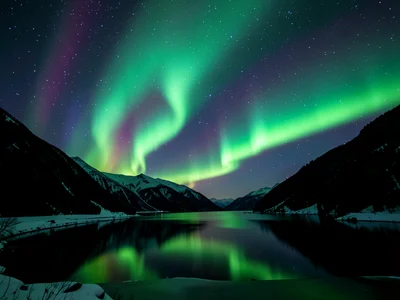 Aurora reflected in still fjord water, mountain silhouette creating dark frame f