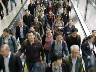 Commuters descending escalator, faces smeared into the collective blur of going 