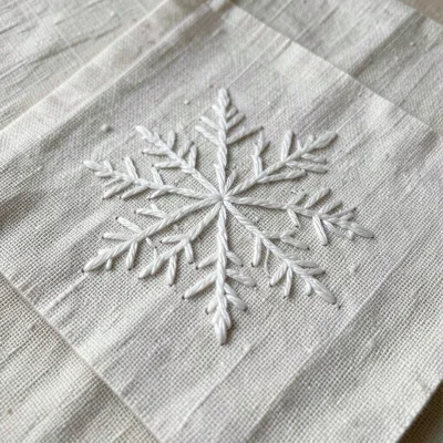 Hand-stitched snowflake pattern on linen napkin, white thread, delicate