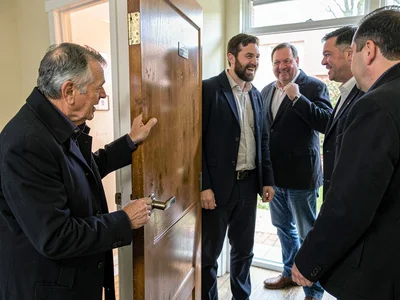 Person putting on coat while hosts hover, the extended goodbye, one hand on door