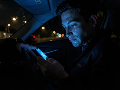 Person reading devastating text message, screen light catching tears, car interi