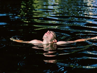 Swimmer emerging from dark water, only shoulders and thrown-back head above surf