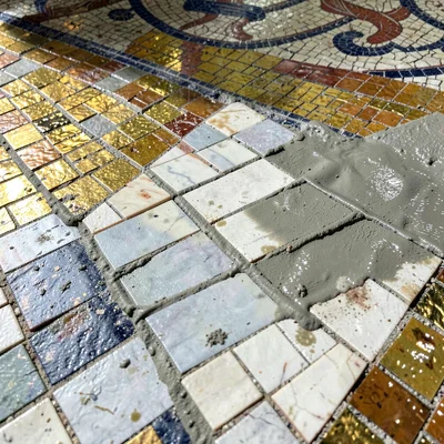 A freshly grouted mosaic panel being cleaned, wet grout haze still on the tile s