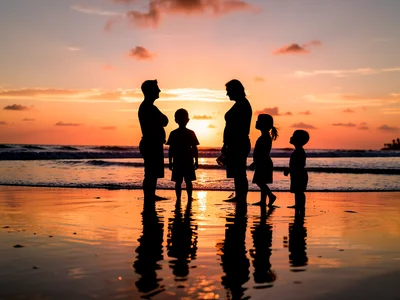 Silhouette of family on beach at sunset, shallow water, reflections, wide shot