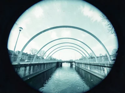 A footbridge over a canal — arcs crossing above, bridge rendered in pale cyanoty