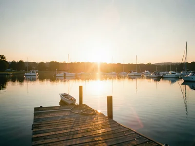 Sunset reflecting off calm lake, dock in foreground, boats moored