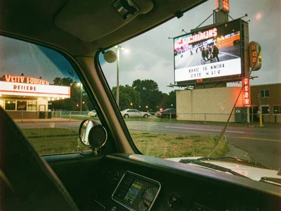 Drive-in movie theater from car hood, speaker on window, screen showing film