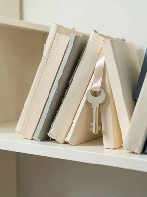 A papercraft library shelf at child-height, hand-cut paper books leaning togethe