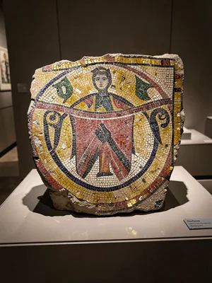 A Roman mosaic fragment displayed on a museum pedestal, tesserae catching overhe
