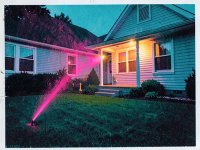 A sprinkler arc misting over a perfect lawn at dusk with the porch light just be