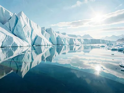 A shallow meltwater layer films the top of a glacier, mirroring the sky so clean