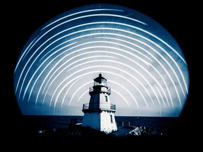A coastal lighthouse with curved sun trail arcs over dark sea horizon