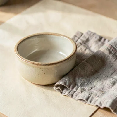 A small ceramic dog bowl with a worn linen napkin folded beside it on warm cream