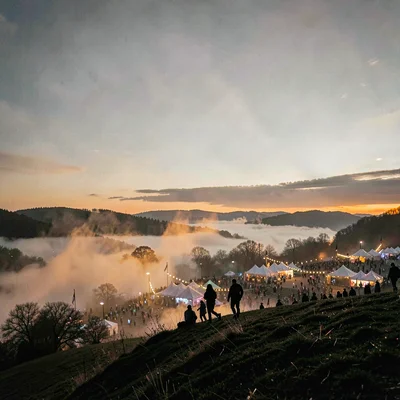 A small group silhouetted on a hillside above the festival grounds at dusk, ambe
