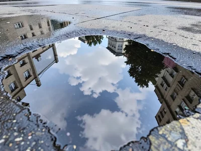 Cloud reflection in large flat puddle on concrete plaza, sky below your feet, pu