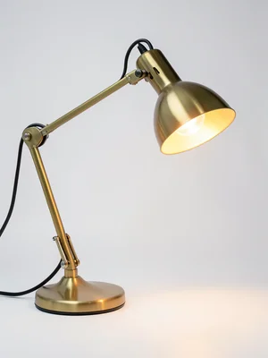 A brass desk lamp, articulated arm, the shade tilted, casting a warm glow on the
